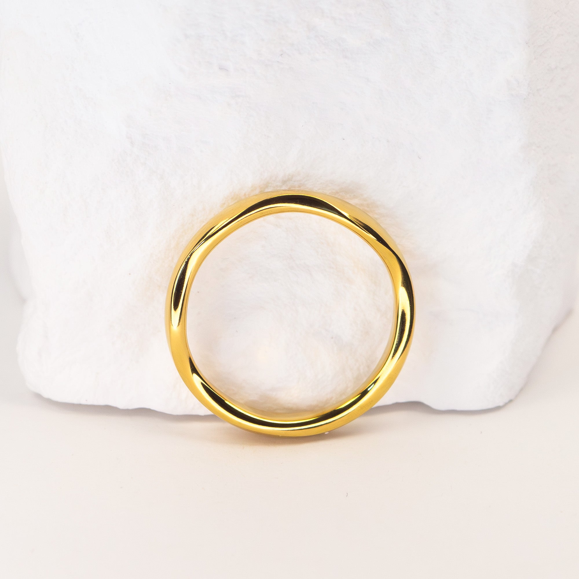 A polished gold ring with a thick, rounded band, displayed on a soft white textured surface.