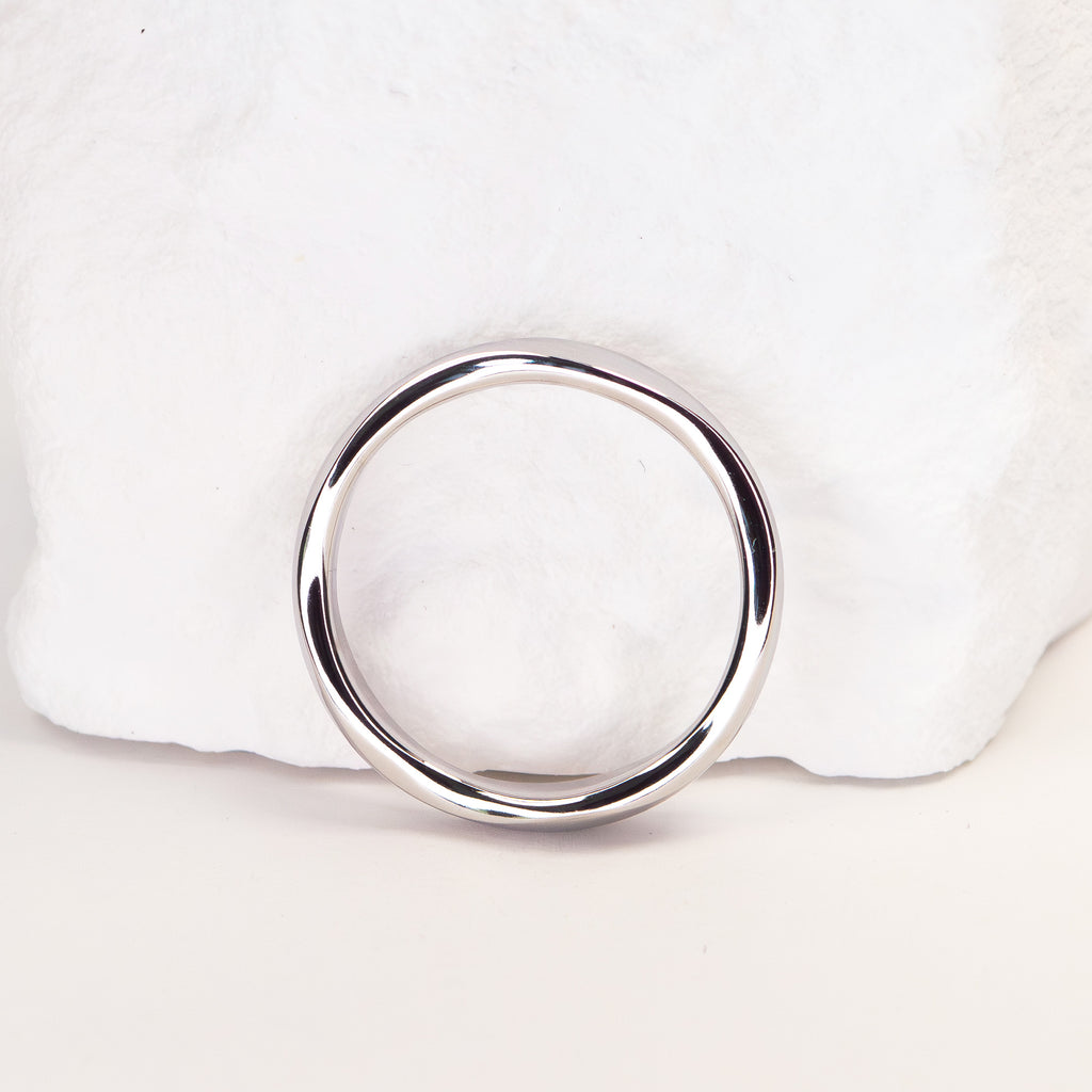 A polished silver-toned metal ring with a thick, rounded band, displayed on a white textured stone prop against a light background.